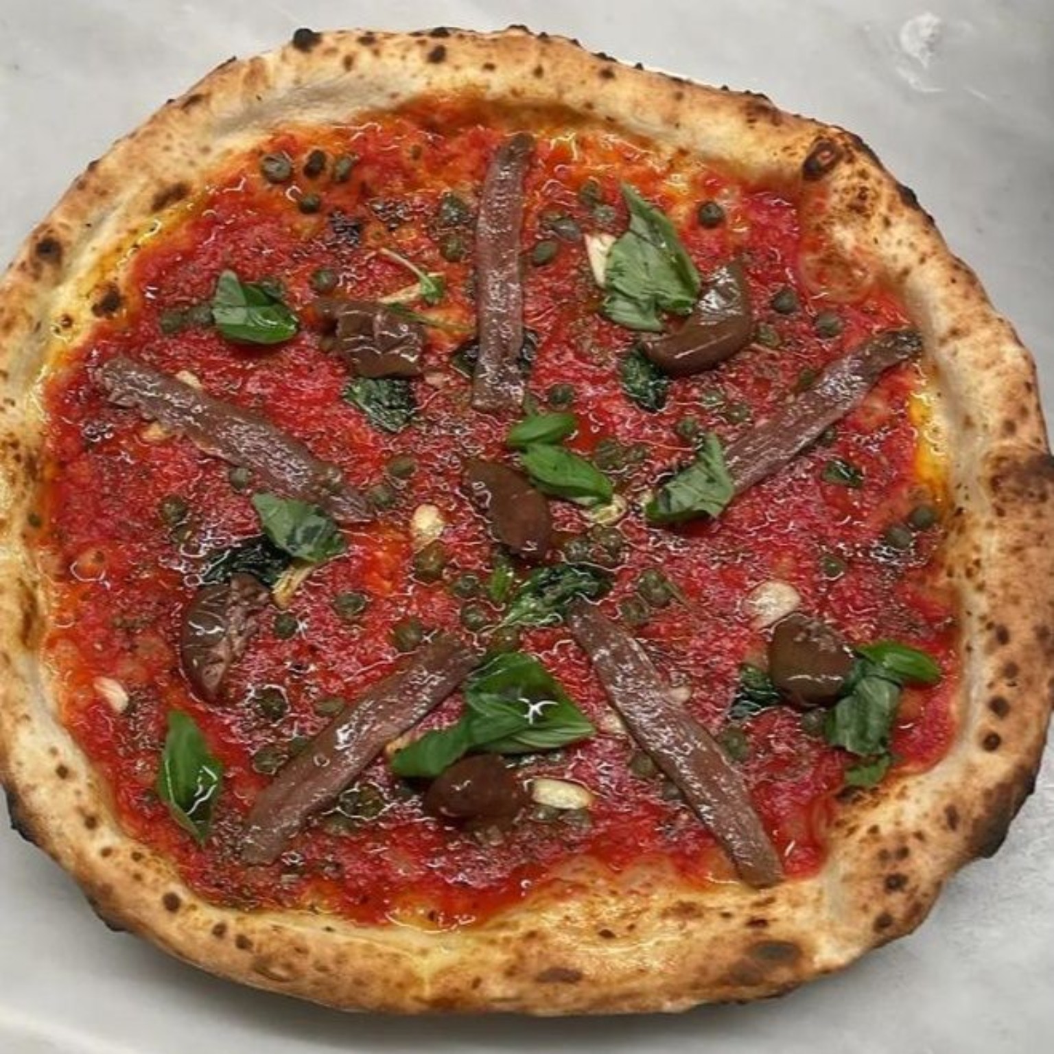 Pizza rossa con acciughe, olive, capperi e basilico